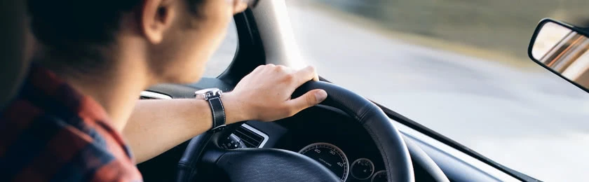 Ein Autofahrer mit Händen am Lenker begibt sich in den Straßenverkehr.