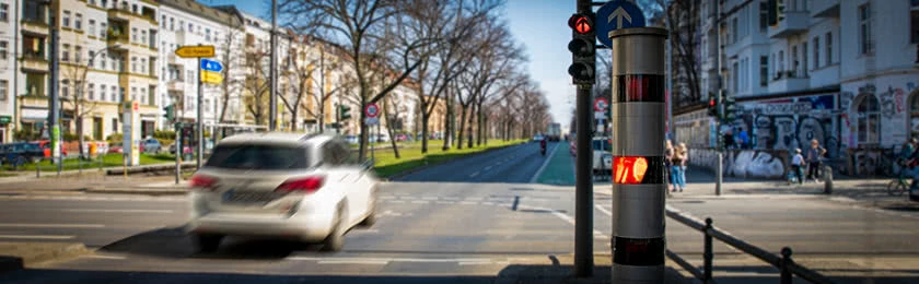 Ein weißes Auto überfährt eine rote Ampel und wird dabei geblitzt.